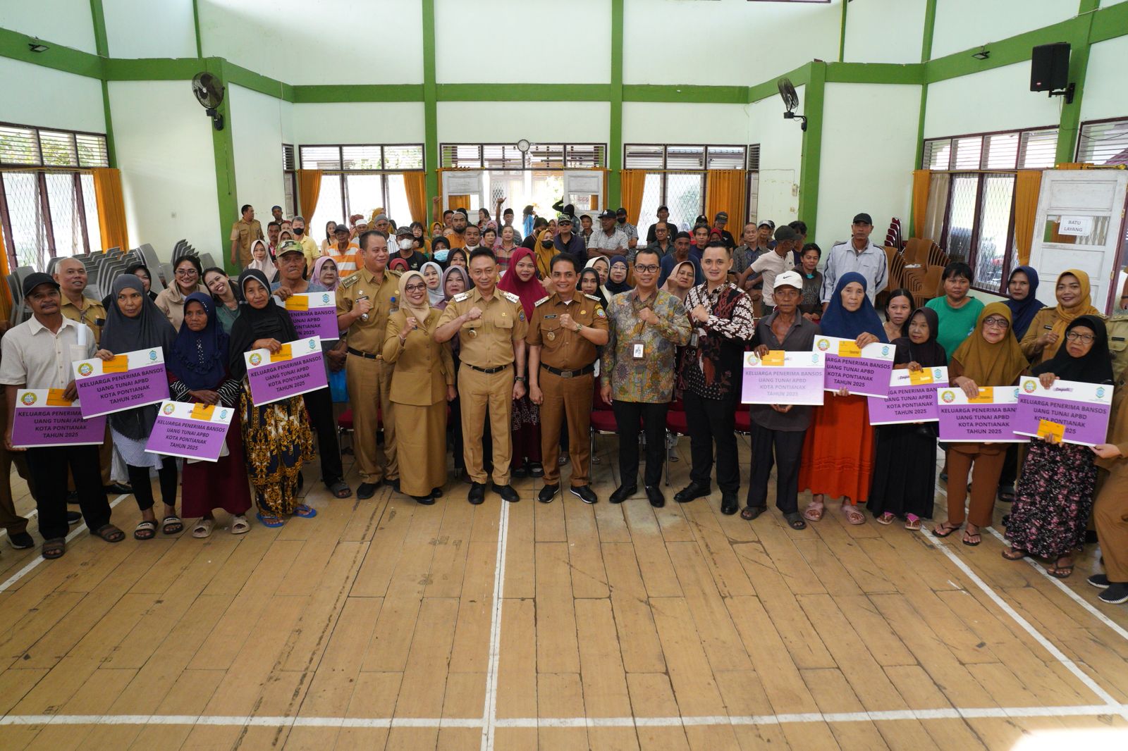 Foto menunjukkan Wali Kota Pontianak, Edi Rusdi Kamtono, bersama pejabat pemerintah dan warga penerima manfaat dalam acara penyerahan Bantuan Sosial Tunai (Bansos Tunai) di Aula Kantor Kecamatan Pontianak Barat pada 11 Maret 2025. Warga memegang papan simbolis penerimaan bantuan dengan suasana penuh keakraban.