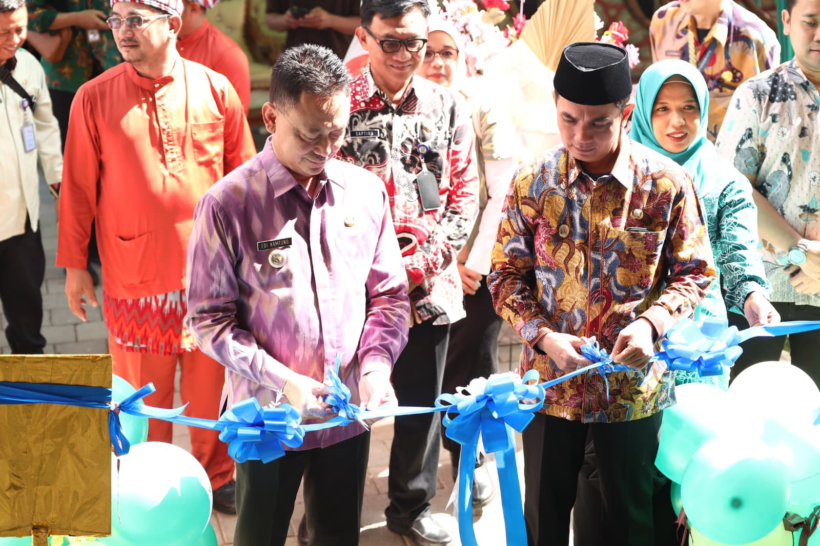 Foto memperlihatkan Wali Kota Pontianak Edi Rusdi Kamtono dan Wakil Wali Kota Bahasan memotong pita berwarna biru dalam acara peresmian fasilitas kesehatan. Mereka mengenakan pakaian batik, dikelilingi oleh beberapa pejabat dan tamu undangan. Balon berwarna hijau terlihat di sekitar area peresmian.