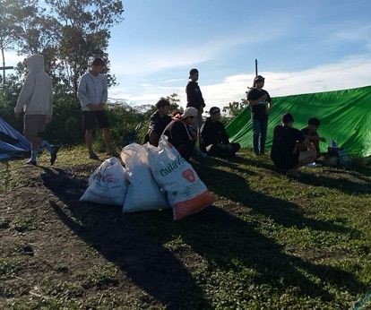 Sekelompok pendaki beristirahat di puncak Bukit Rentap, Sintang, dengan beberapa kantong sampah berisi plastik di sekitar mereka.