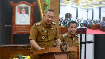 Bupati Ketapang, Alexander Wilyo, mengenakan seragam dinas cokelat muda, berbicara di podium dengan logo Garuda Pancasila