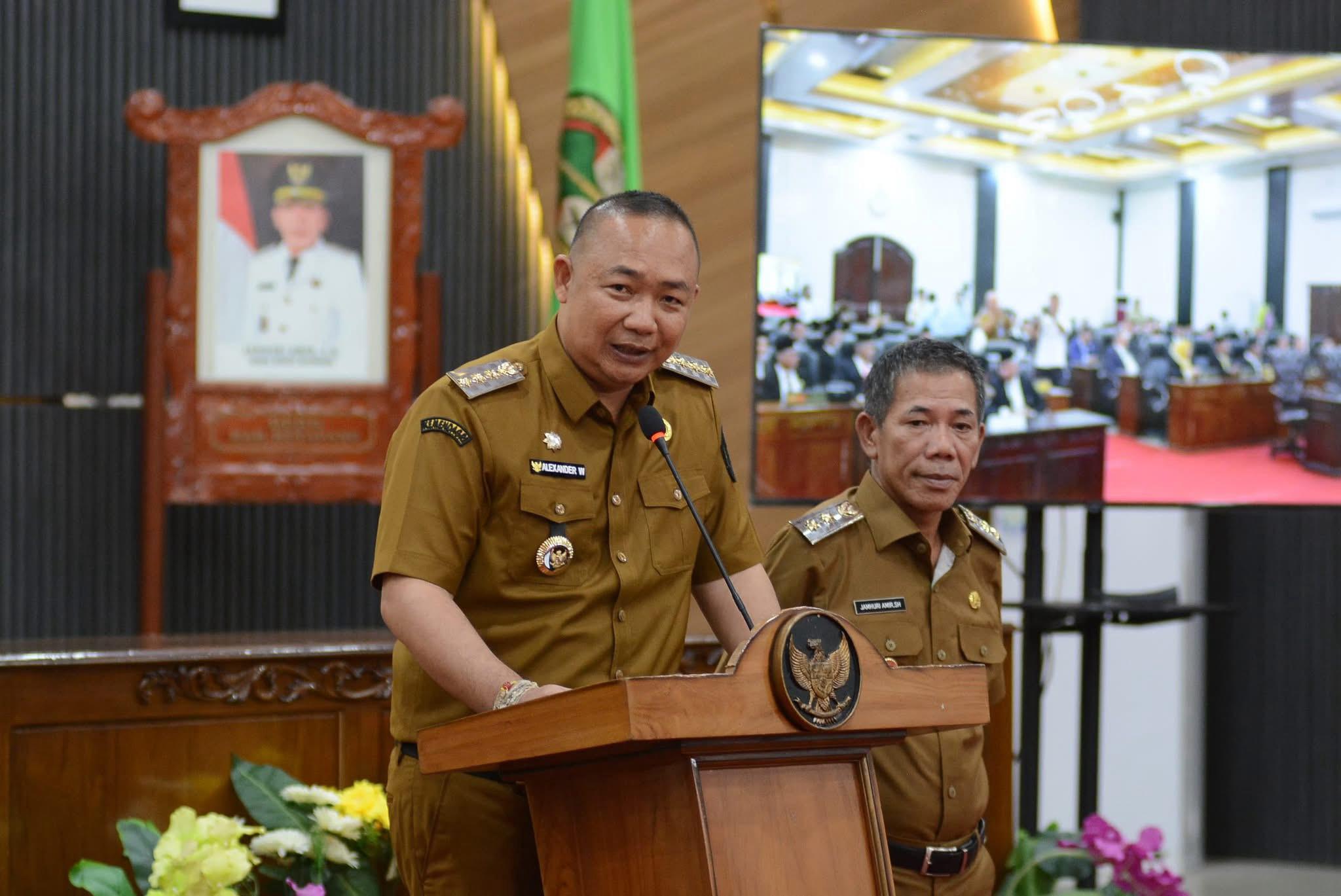 Bupati Ketapang, Alexander Wilyo, mengenakan seragam dinas cokelat muda, berbicara di podium dengan logo Garuda Pancasila