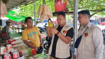 Tiga petugas Satgas Pangan Polres Ketapang mengenakan rompi bertugas melakukan inspeksi minyak goreng Minyakita di sebuah kios pasar. Salah satu petugas memegang botol minyak untuk diperiksa, sementara pedagang dengan kaos kuning berdiri di sampingnya.