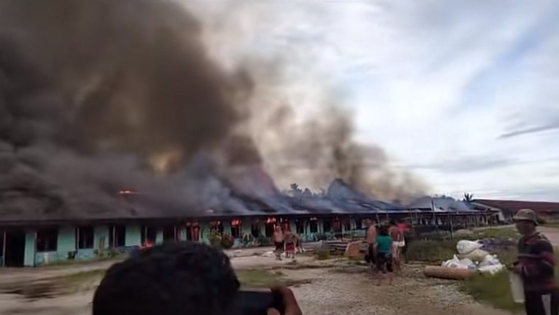 Asap hitam tebal membubung dari Rumah Betang di Desa Kekurak, Kapuas Hulu, yang terbakar. Beberapa warga terlihat menyaksikan kebakaran dari kejauhan, sementara lainnya mencoba menyelamatkan barang-barang.