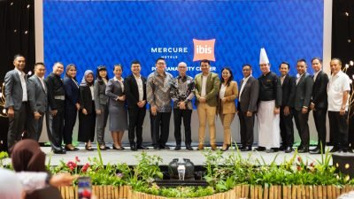 "Kelompok besar staf hotel Mercure dan ibis Pontianak City Center berpose di panggung dengan latar belakang layar besar berlogo hotel. Di tengah terlihat General Manager Ulysses Jeffrey dan Director of Operations Accor Indonesia Endrian Hananto."
