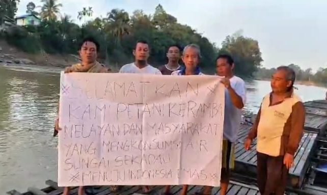 "Sejumlah petani keramba dan masyarakat membentangkan spanduk di atas rakit di Sungai Sekadau. Spanduk tersebut berisi seruan untuk menyelamatkan mereka dari dampak pencemaran sungai yang diduga akibat limbah penambangan emas tanpa izin (PETI), yang telah merugikan mata pencaharian dan mengancam sumber air konsumsi warga.