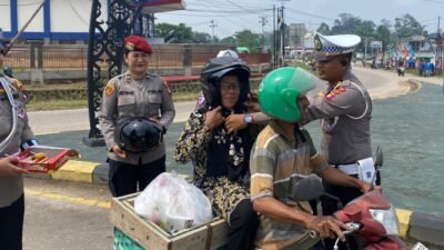 Seorang petugas dari Polres Sekadau dengan ramah memasangkan helm SNI gratis kepada seorang pengendara sepeda motor di Bundaran Tugu PKK, sebagai bagian dari aksi simpatik perayaan Hari Jadi Polwan ke-77.
