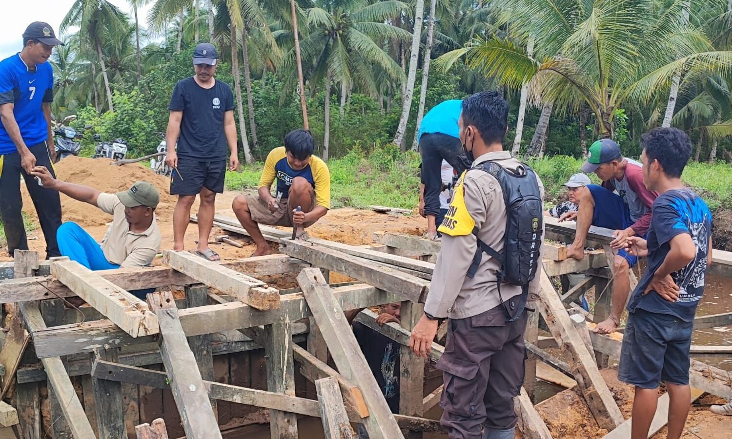"Warga Dusun Pancuran, Kayong Utara, bergotong royong memperbaiki jembatan rusak demi keselamatan. Sinergi aparat desa dan warga perbaiki infrastruktur. "