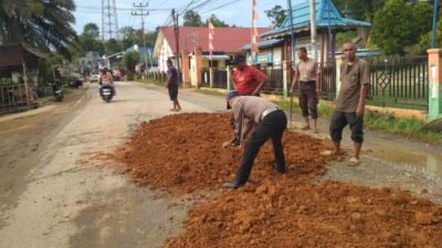 Anggota Polsek Tayan Hilir bersama warga saat melakukan kerja bakti menambal jalan berlubang di Jalan Pembangunan, Desa Kawat, Senin (17/11/2025).