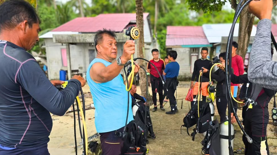 Sejumlah peserta, termasuk seorang pria berbaju biru, sedang antusias memeriksa dan mempersiapkan peralatan selam dalam pelatihan yang digelar DKP Kalbar di Desa Pelapis, Kepulauan Karimata. (Dok. HO/Faktakalbar.id)