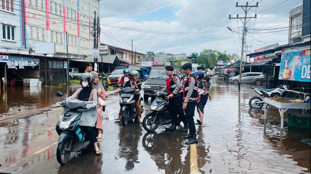 personel Sat Samapta Polres Ketapang sedang membantu mendorong sepeda motor warga yang terjebak genangan banjir di jalan raya. (Dok. HO/Faktakalbar.id)