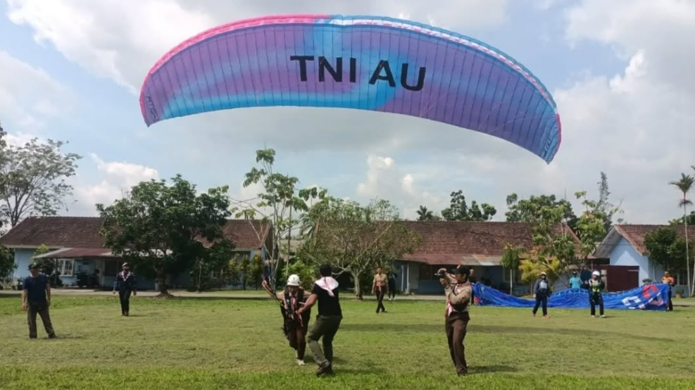 Seorang peserta pelatihan paralayang PL-1 sedang berlatih Ground Handling menggunakan parasut bertuliskan "TNI AU" di lapangan Lanud Supadio, diawasi oleh instruktur dan anggota Saka Dirgantara. (Dok. Instagram/@lanud_supadio)