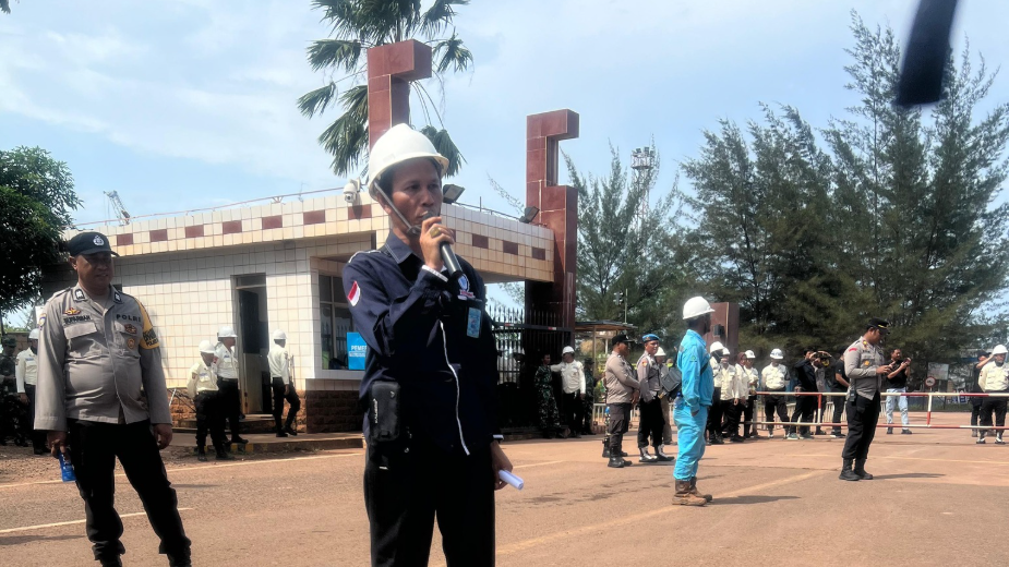 Seorang perwakilan serikat buruh (mengenakan helm putih) sedang berorasi menggunakan mikrofon di hadapan massa aksi mogok kerja dan aparat kepolisian di gerbang PT WHW. (Dok. Ist)