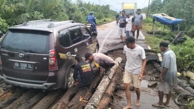 "Akibat kayu penyangga lapuk, sebuah mobil Avanza terperosok di jembatan Desa Teluk Melano, Simpang Hilir. Polisi dan warga bahu-membahu lakukan evakuasi."
