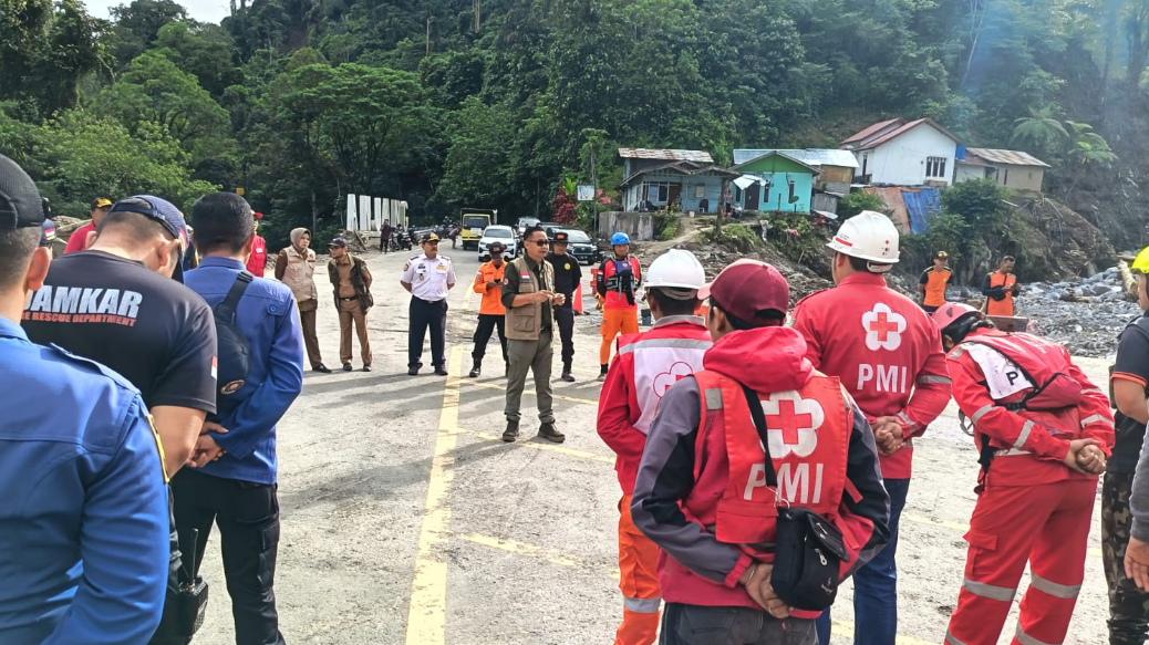 Personel tim SAR gabungan mendengarkan arahan dari pejabat BNPB saat apel pagi di lokasi terdampak longsor Padang Panjang dengan latar belakang kerusakan infrastruktur. (Dok. HO/Faktakalbar.id)