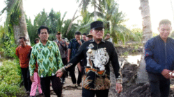 Bupati Sujiwo mengenakan kemeja hitam bermotif harimau dan topi hitam berjalan kaki meninjau lokasi jembatan di pedesaan didampingi warga dan perangkat desa. (Dok. HO/Faktakalbar.id)