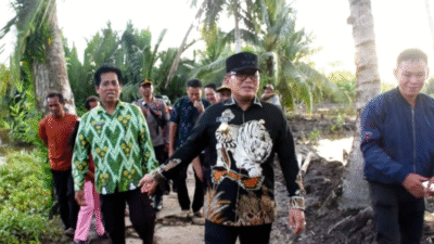 Bupati Sujiwo mengenakan kemeja hitam bermotif harimau dan topi hitam berjalan kaki meninjau lokasi jembatan di pedesaan didampingi warga dan perangkat desa. (Dok. HO/Faktakalbar.id)