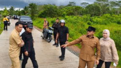Bupati Sujiwo mengenakan kacamata hitam dan seragam dinas menunjuk ke arah jalan beton saat inspeksi perbaikan infrastruktur jalan di Sungai Ambawang. (Dok. HO/Faktakalbar.id)