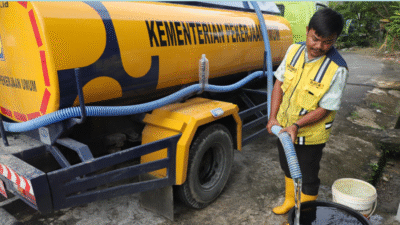 Petugas berseragam kuning dari Dinas Pekerjaan Umum mengisi ember warga dengan air bersih melalui selang dari truk tangki air berwarna kuning. (Dok. BNPB)