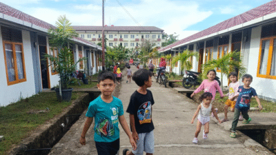 Anak-anak bermain ceria di jalan setapak antara deretan rumah hunian sementara (huntara) berwarna putih dengan atap merah marun. (Dok. BNPB)