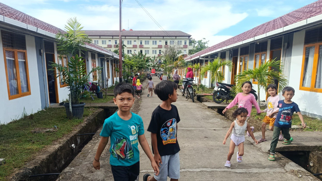 Anak-anak bermain ceria di jalan setapak antara deretan rumah hunian sementara (huntara) berwarna putih dengan atap merah marun. (Dok. BNPB)
