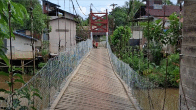 Jembatan gantung kayu dengan pagar kawat terlihat miring dan rusak di atas sungai yang keruh, membahayakan penyeberang. (Dok. Facebook/Ria Mahap)