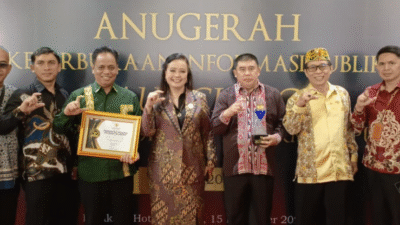 Sekelompok pejabat pria dan wanita memegang piagam penghargaan dan trofi Anugerah Keterbukaan Informasi Publik dengan latar belakang backdrop hitam emas. (Dok. HO/Faktakalbar.id)