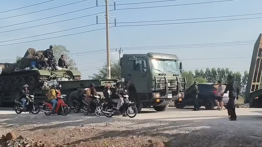 Truk trailer militer berwarna hijau mengangkut tank T-55 melintas di jalan raya berpapasan dengan warga sipil saat mobilisasi pasukan Kamboja. (Dok. Ist)