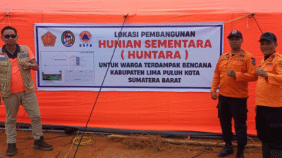 Tiga petugas berseragam oranye BPBD dan BNPB berfoto di depan spanduk oranye bertuliskan Lokasi Pembangunan Hunian Sementara (Huntara) Kabupaten Lima Puluh Kota. (Dok. HO/Faktakalbar.id)