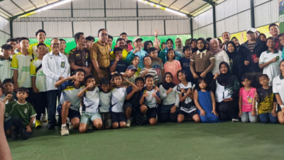Gubernur Ria Norsan mengenakan topi dan jaket olahraga biru berfoto bersama puluhan anak-anak peserta turnamen tenis di dalam lapangan semi indoor. (Dok. HO/Faktakalbar.id)