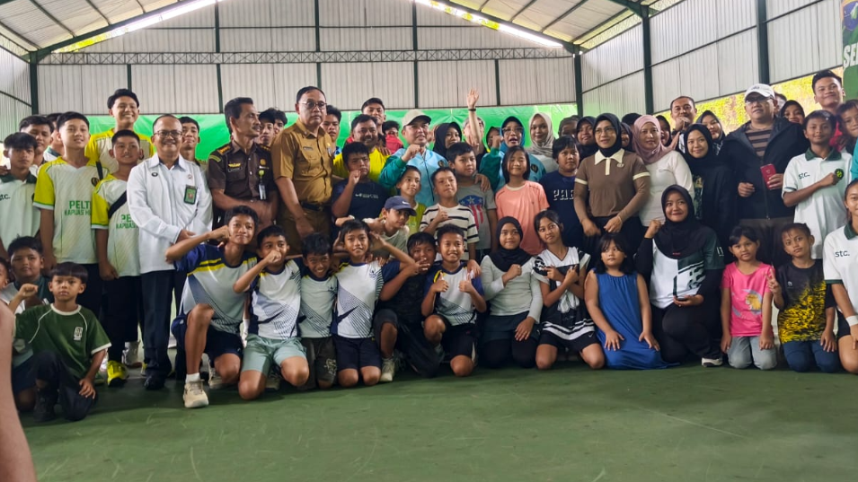 Gubernur Ria Norsan mengenakan topi dan jaket olahraga biru berfoto bersama puluhan anak-anak peserta turnamen tenis di dalam lapangan semi indoor. (Dok. HO/Faktakalbar.id)