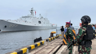 Prajurit Marinir TNI AL bersenjata lengkap berdiri menjaga area dermaga dengan latar belakang kapal perang besar berwarna abu-abu bernomor lambung 989. (Dok. HO/Faktakalbar.id)
