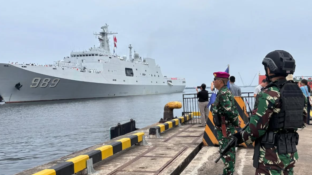 Prajurit Marinir TNI AL bersenjata lengkap berdiri menjaga area dermaga dengan latar belakang kapal perang besar berwarna abu-abu bernomor lambung 989. (Dok. HO/Faktakalbar.id)