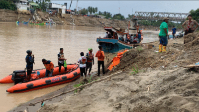 Perahu karet oranye bertuliskan BNPB mengangkut penumpang menyeberangi sungai cokelat keruh di dekat reruntuhan jembatan beton yang putus. (Dok. BNPB)