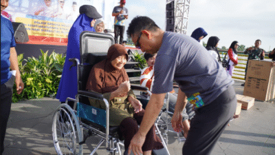Wali Kota Pontianak Edi Kamtono membungkuk memperbaiki pijakan kaki kursi roda untuk seorang nenek lansia berhijab cokelat di acara outdoor. (Dok. HO/Faktakalbar.id)