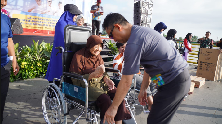Wali Kota Pontianak Edi Kamtono membungkuk memperbaiki pijakan kaki kursi roda untuk seorang nenek lansia berhijab cokelat di acara outdoor. (Dok. HO/Faktakalbar.id)
