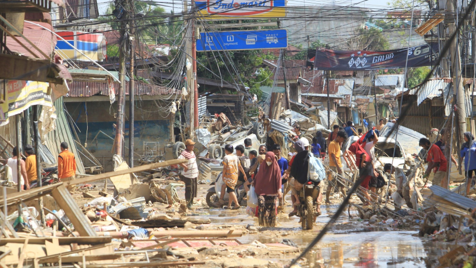 Warga Aceh Tamiang memanggul kasur dan harta benda yang tersisa melewati jalan berlumpur dan rusak parah akibat banjir bandang dan longsor. (Dok. ANTARA)
