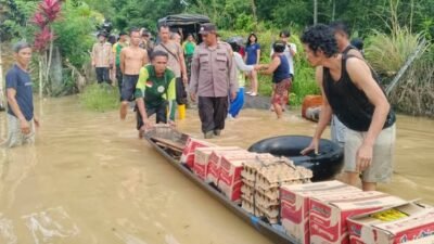 Personel kepolisian saat menyalurkan bantuan logistik kepada warga yang terdampak banjir akibat luapan Sungai Sekayam di Kecamatan Entikong, Jumat (9/1).