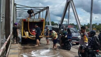 Petugas Damkar dibantu kepolisian saat melakukan penyemprotan air untuk membersihkan sisa tumpahan solar yang menyebabkan jalan licin dan pengendara terjatuh di Jembatan Melawi, Sabtu (3/1).