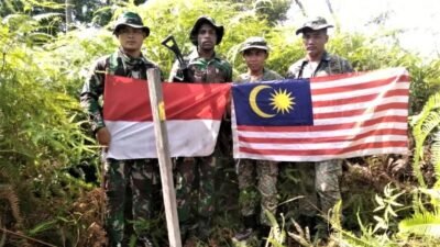 Personel TNI dan Tentara Diraja Malaysia berfoto bersama memegang bendera kedua negara di patok perbatasan Indonesia-Malaysia di tengah hutan. (Dok. HO/Faktakalbar.id)