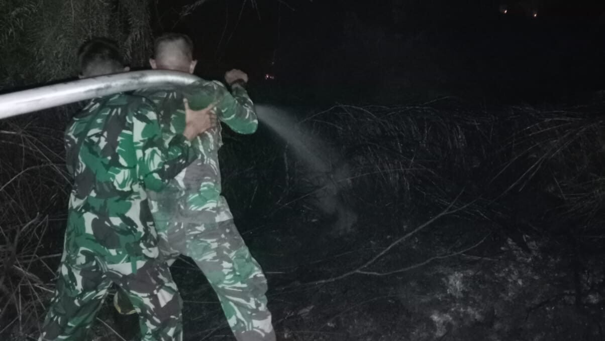 Personel Denmadam XII/Tanjungpura saat memadamkan api yang membakar lahan gambut di dekat pemukiman warga, Minggu (18/1) dini hari.