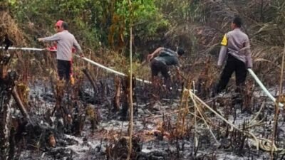 Personel Polsek Manis Mata dibantu warga saat melakukan upaya pemadaman dan pendinginan di lokasi kebakaran lahan Dusun Keladi, Desa Ratu Elok, Senin (26/1).