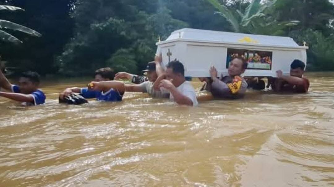 Anggota Polsek Entikong bersama warga setempat saat menggotong keranda jenazah menerobos banjir setinggi 1,5 meter di Desa Nekan, Minggu (11/1).