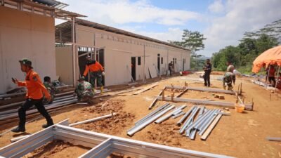 Sejumlah personel TNI dan petugas berbaju oranye sedang bekerja merakit rangka baja ringan untuk pembangunan hunian sementara (huntara) di area tanah lapang yang sedang dikerjakan. (Dok. HO/Faktakalbar.id)
