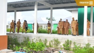 Wakil Bupati Kayong Utara Amru Chanwari mengenakan seragam dinas khaki dan topi memimpin rombongan meninjau lokasi konstruksi bangunan rumah sakit dengan berjalan di atas titian kayu. (Dok. HO/Faktakalbar.id)