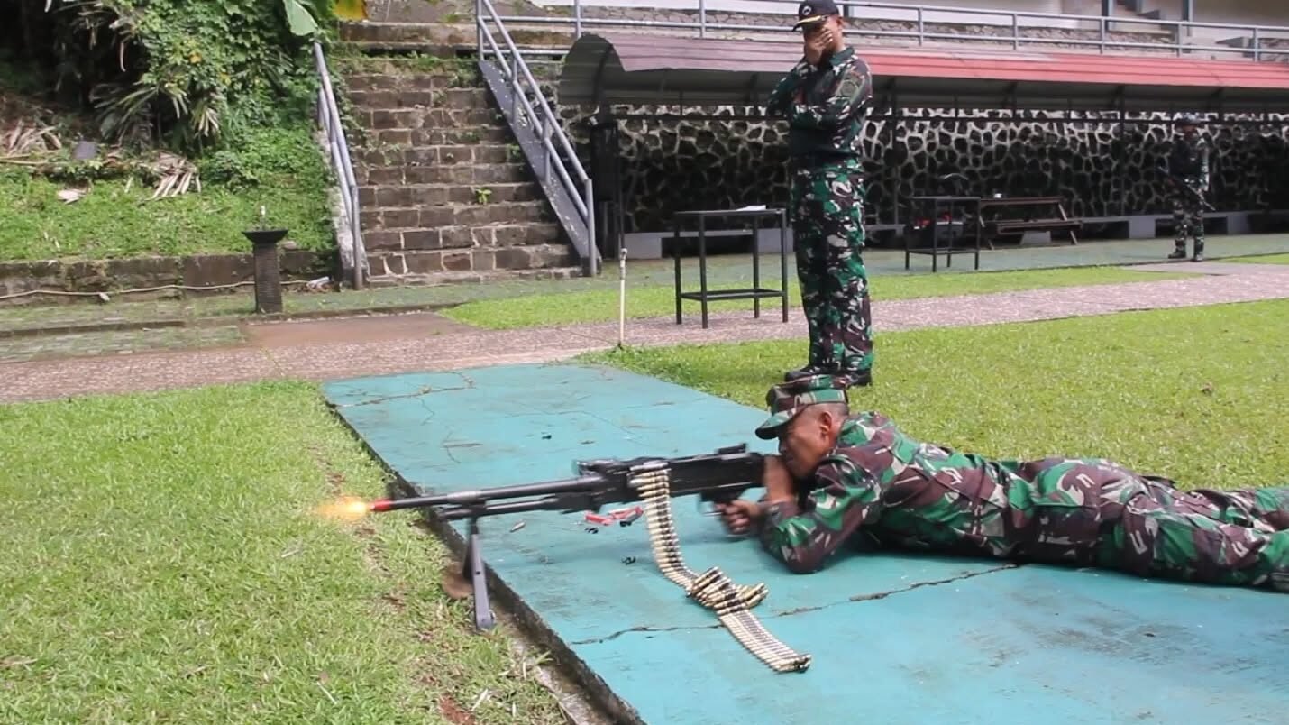 Seorang prajurit Marinir berseragam loreng lengkap melakukan penembakan senjata mesin otomatis dalam posisi tiarap dengan mengeluarkan api laras, diawasi oleh instruktur di lapangan tembak terbuka. (Dok. HO/Faktakalbar.id)