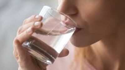 Ilustrasi seseorang mengonsumsi air putih untuk mencegah risiko komplikasi penyakit akibat kekurangan cairan dan elektrolit.
