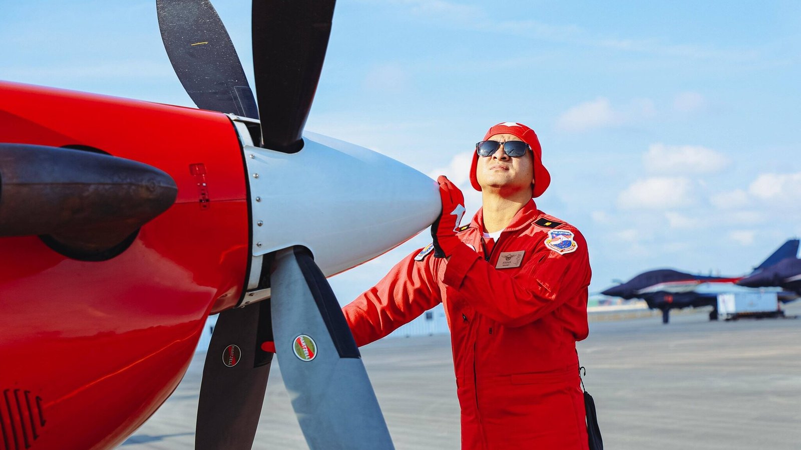 Seorang penerbang Jupiter Aerobatic Team (JAT) TNI AU berkostum merah sedang melakukan pengecekan teknis pada bagian depan (propeller) pesawat latih KT-1B Woongbi di Bandara Changi, Singapura. (Dok. HO/Faktakalbar.id)