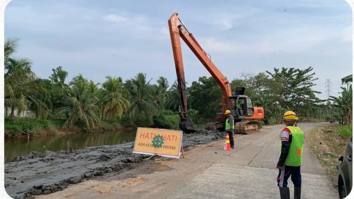 Alat berat ekskavator berwarna oranye sedang melakukan pengerukan tanah di tepi jalan untuk persiapan pembangunan turap di Desa Sungai Itik, Kubu Raya, diawasi oleh pekerja proyek. (Dok. HO/Faktakalbar.id)