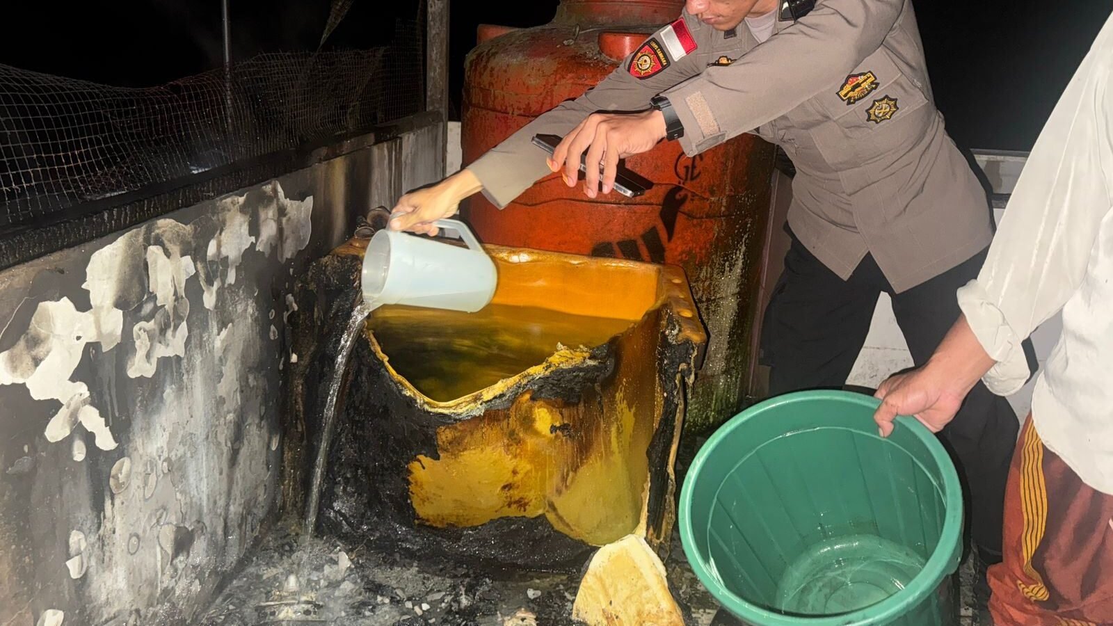 Petugas kepolisian saat memeriksa sisa puing mesin cuci yang hangus terbakar di lantai tiga rumah warga Dusun Entikong Tapang, Senin (9/2/2026).