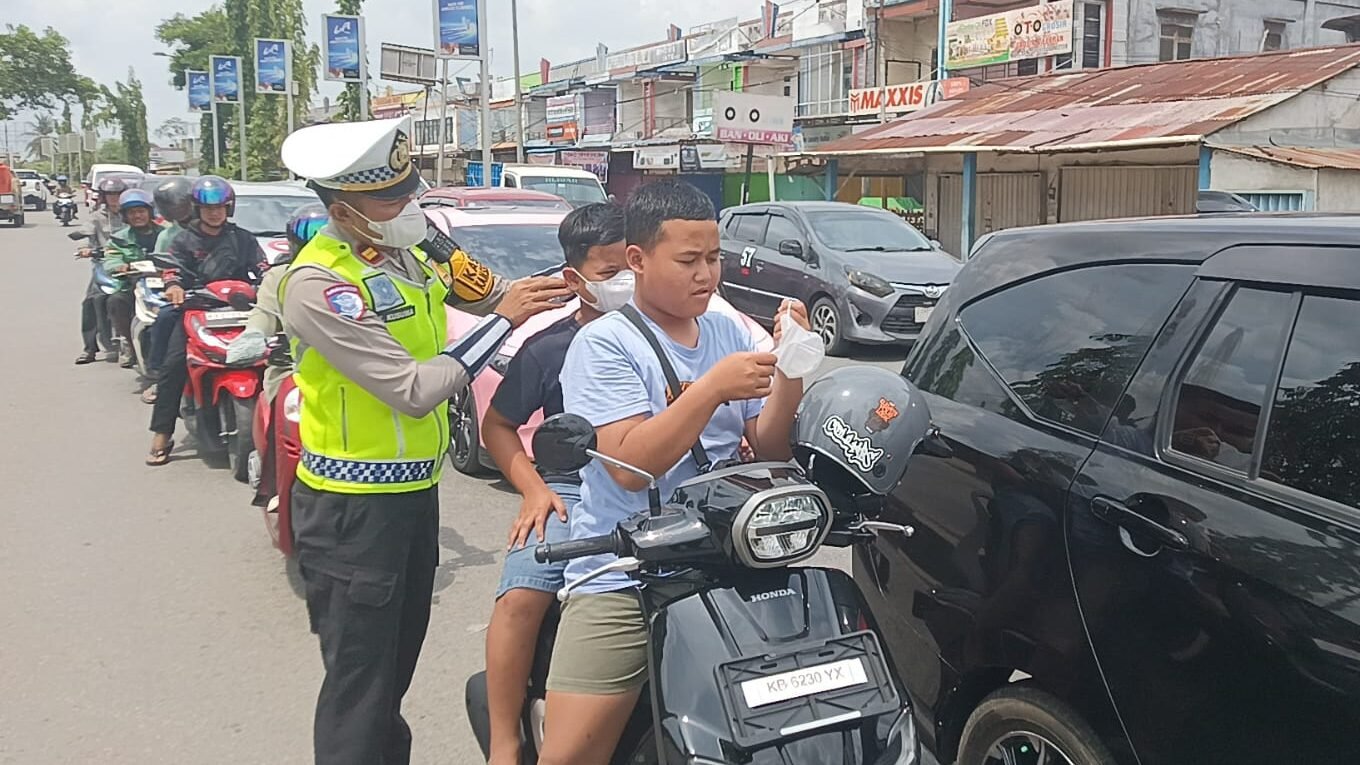 Personel kepolisian saat memberikan masker secara gratis kepada pengendara motor di depan Pos Pelayanan Operasi Liong Kapuas, Kabupaten Kubu Raya, guna melindungi warga dari dampak asap Karhutla, Selasa (17/2/2026).